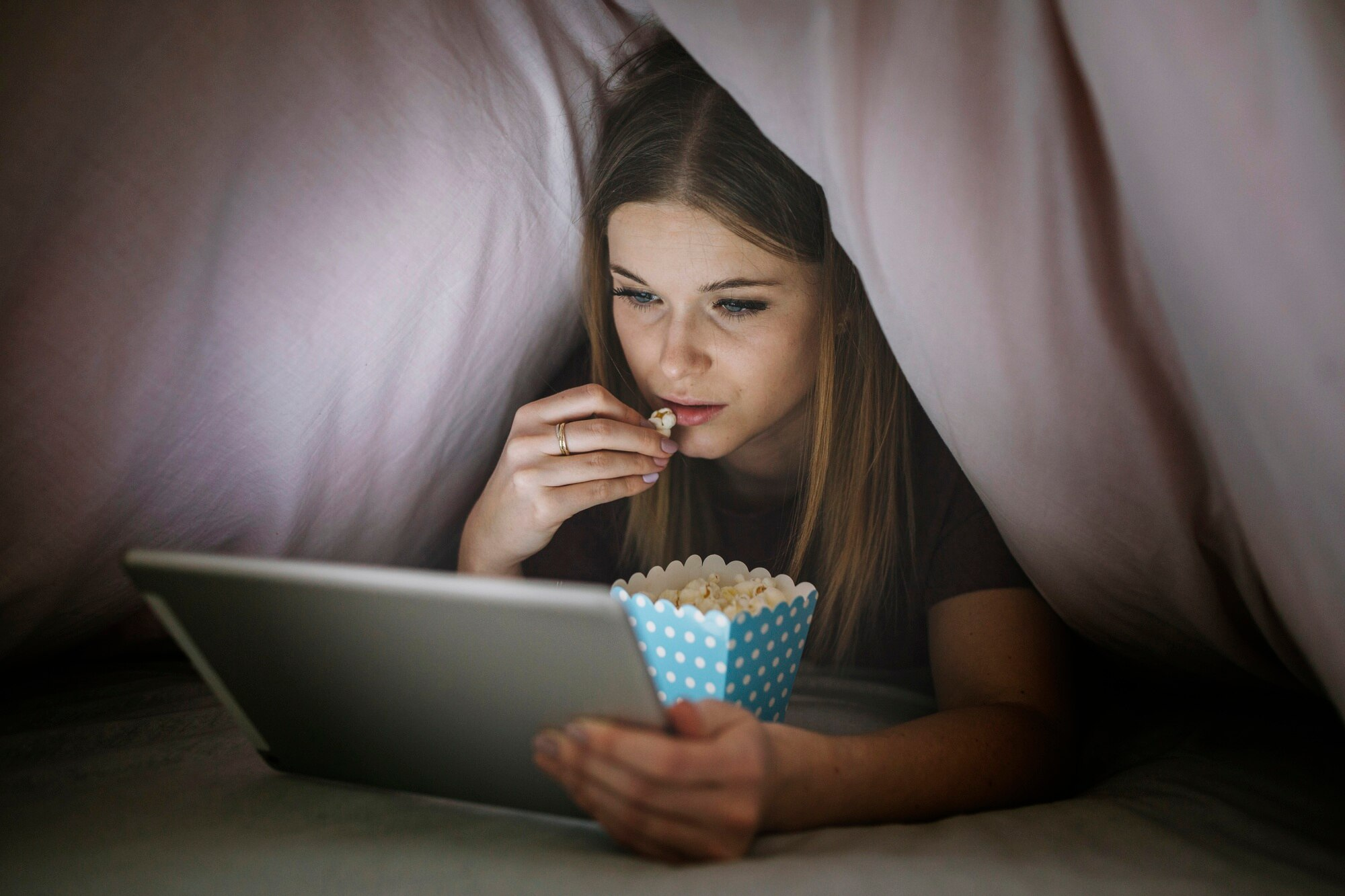 Kobieta oglada film pod koldra na laptopie