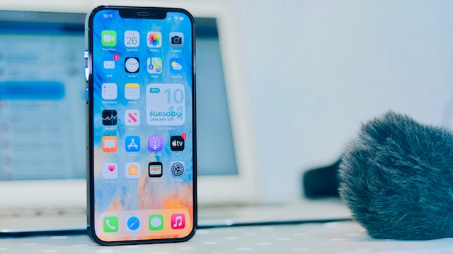 Telefon komórkowy z włączonym wyświetlaczem, w tle laptop